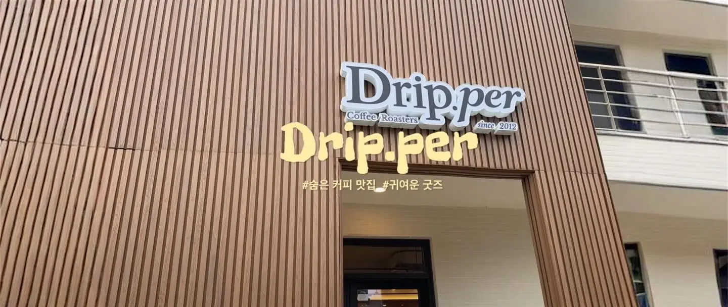 우드 외벽에 붙은 커피드립퍼 간판. Drip.per Coffee Roasters 라고 적혀 있고 아래로 출입문이 보인다.